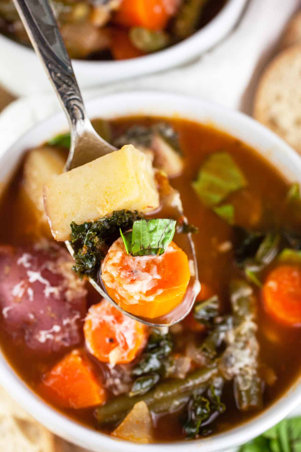 Spoonful of vegetable soup lifted from white bowl.