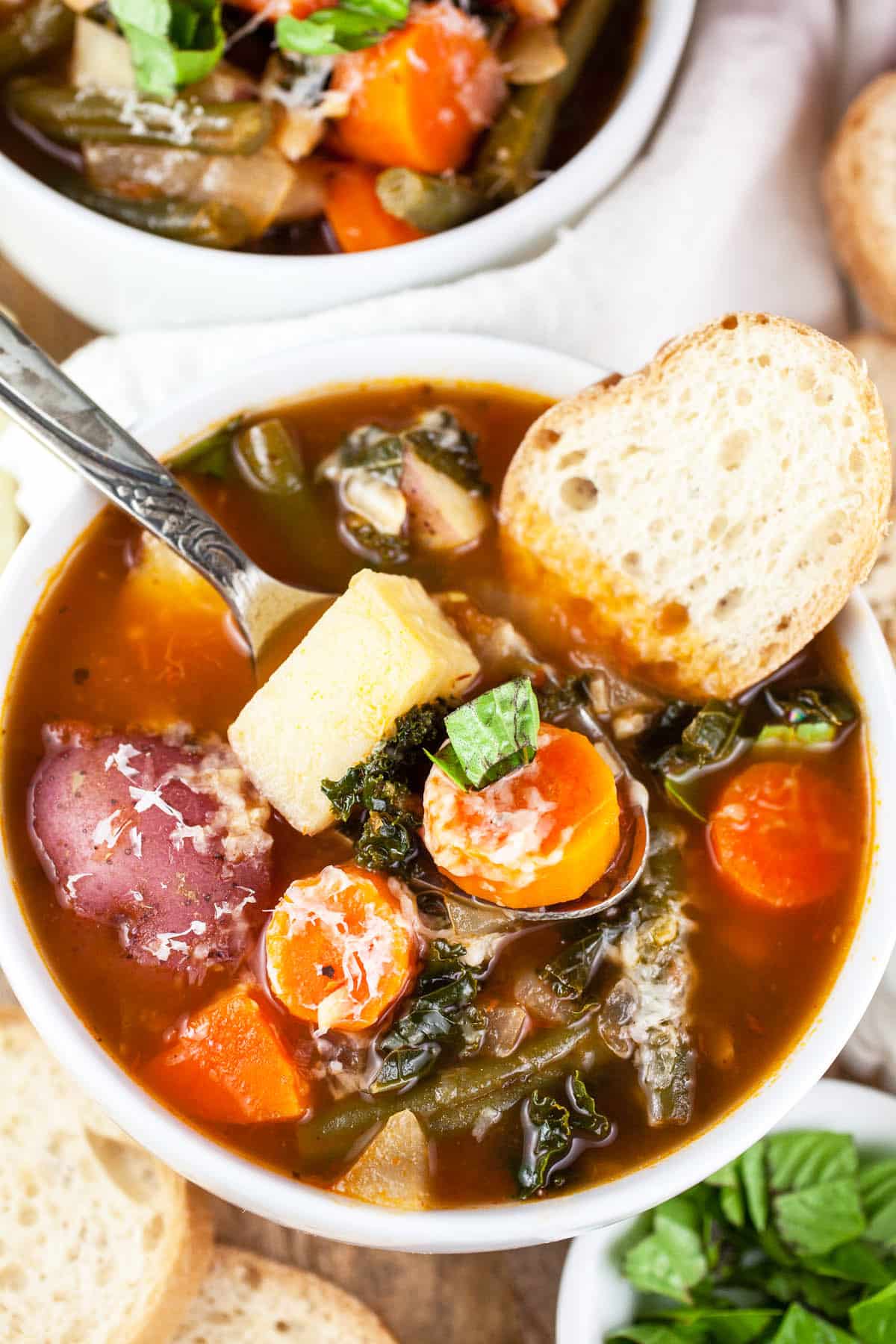 Chunky vegetable soup with bread in white bowl.