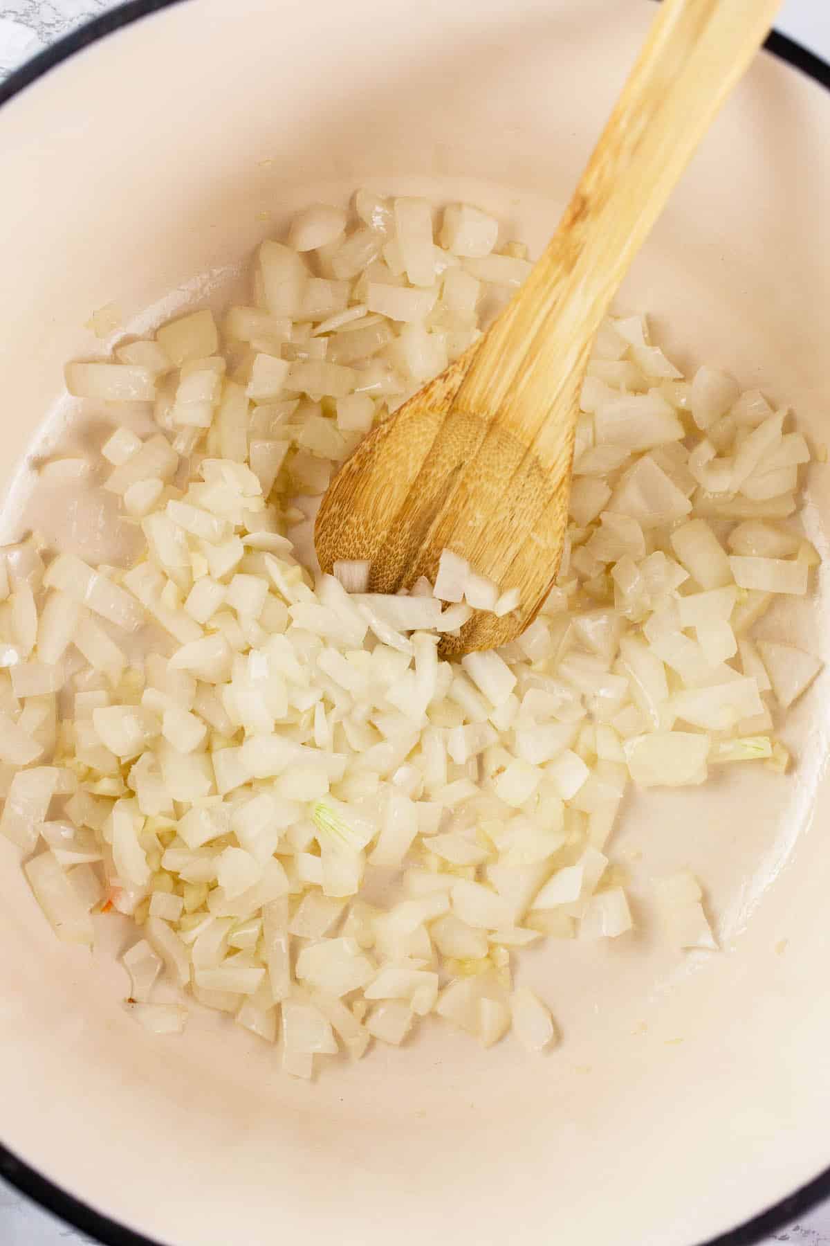 Minced garlic and onions sautéed in Dutch oven with wooden spoon.