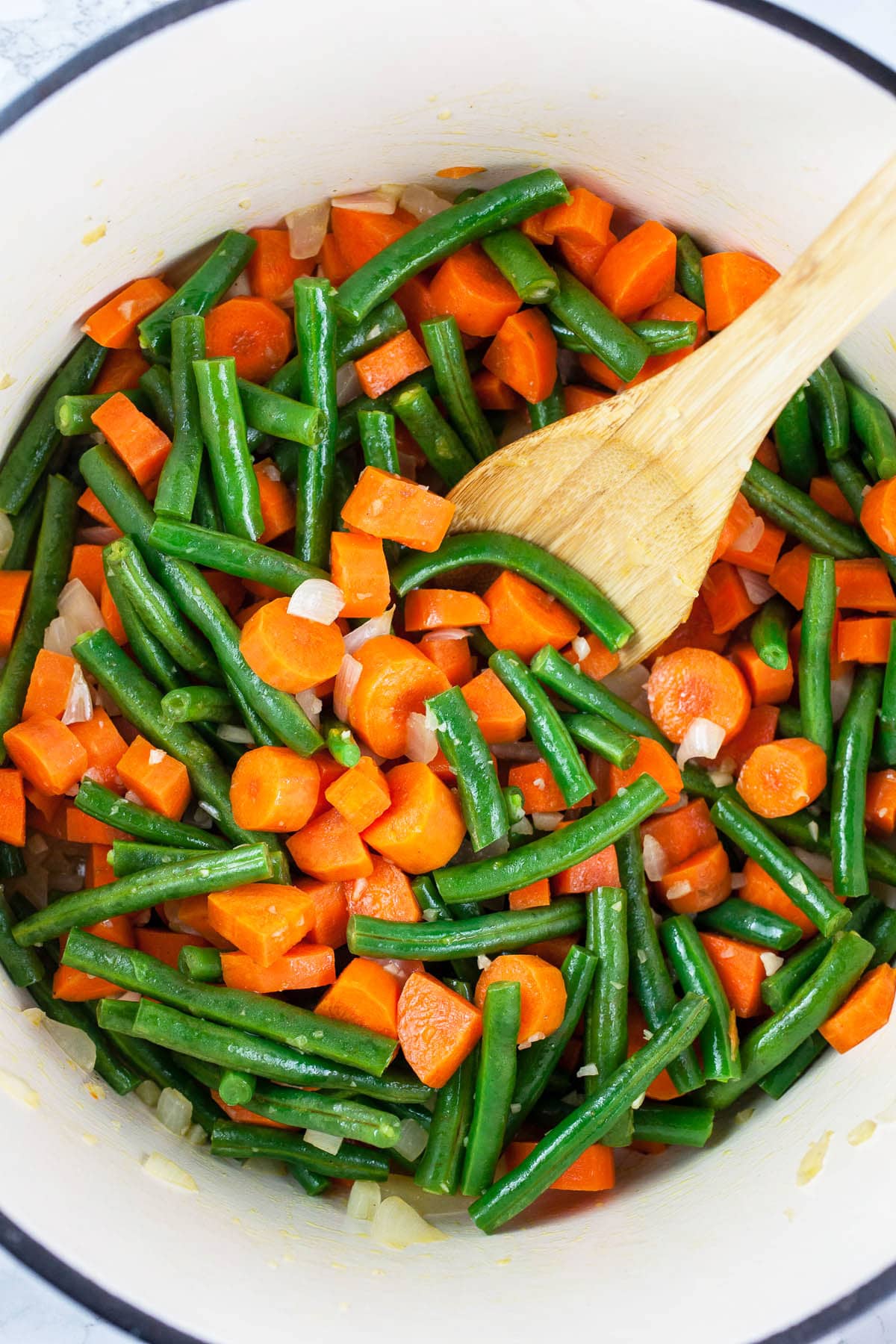 Green beans and carrots sautéed in Dutch oven with wooden spoon.