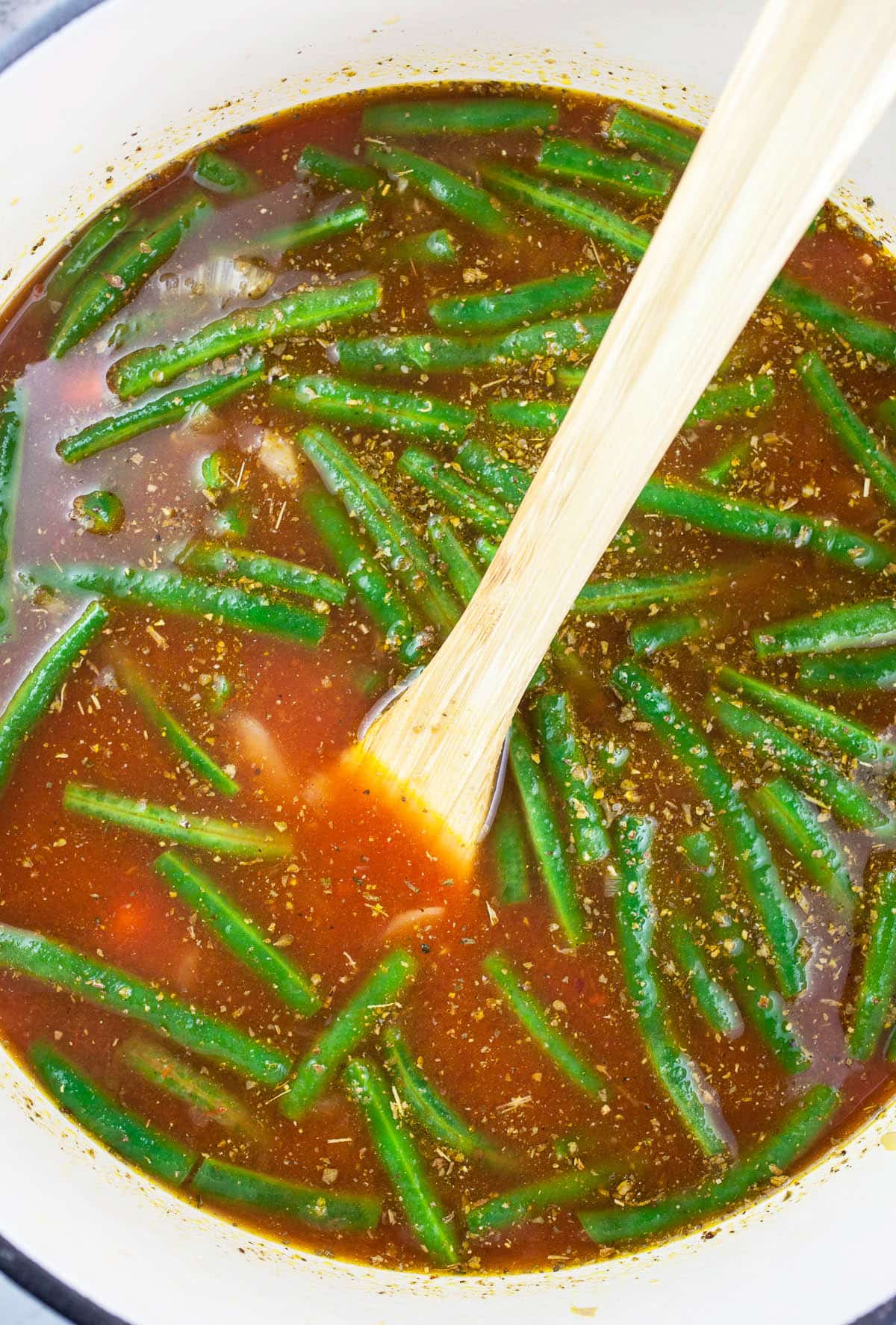 Uncooked vegetable soup in Dutch oven with wooden spoon.