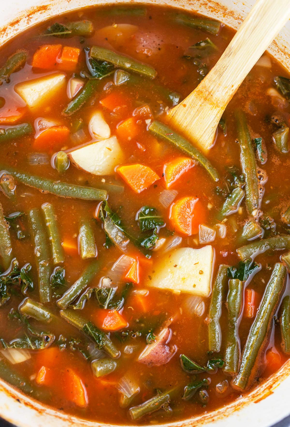 Cooked vegetable soup in Dutch oven with wooden spoon.