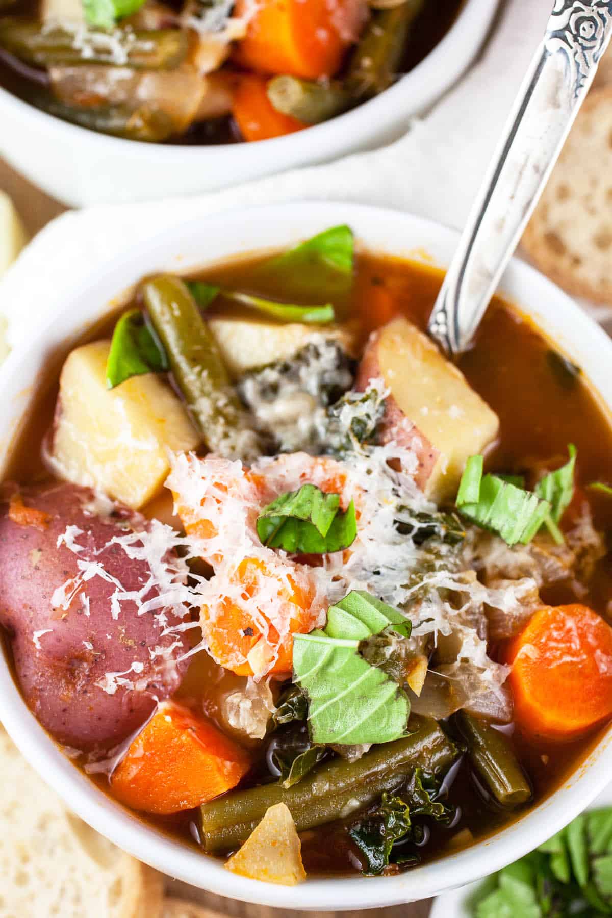 Chunky vegetable soup with Parmesan cheese in white bowl with spoon.