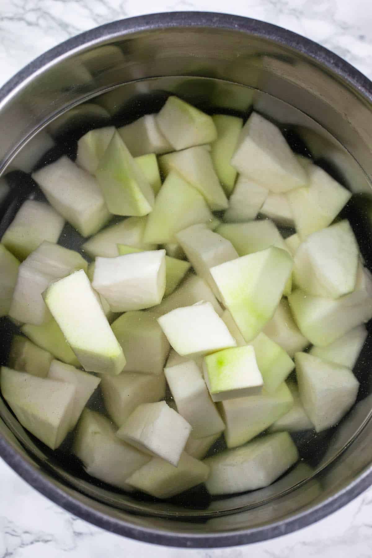 Uncooked kohlrabi chunks in pot of water.