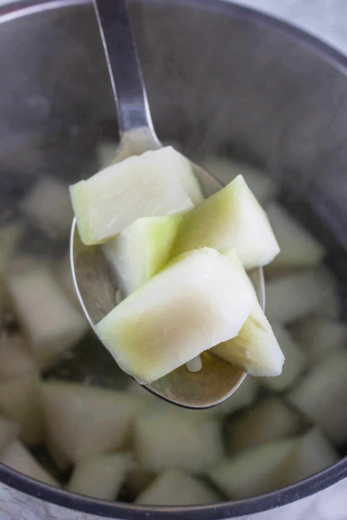 Cooked kohlrabi chunks on metal spoon lifted from pot of water.