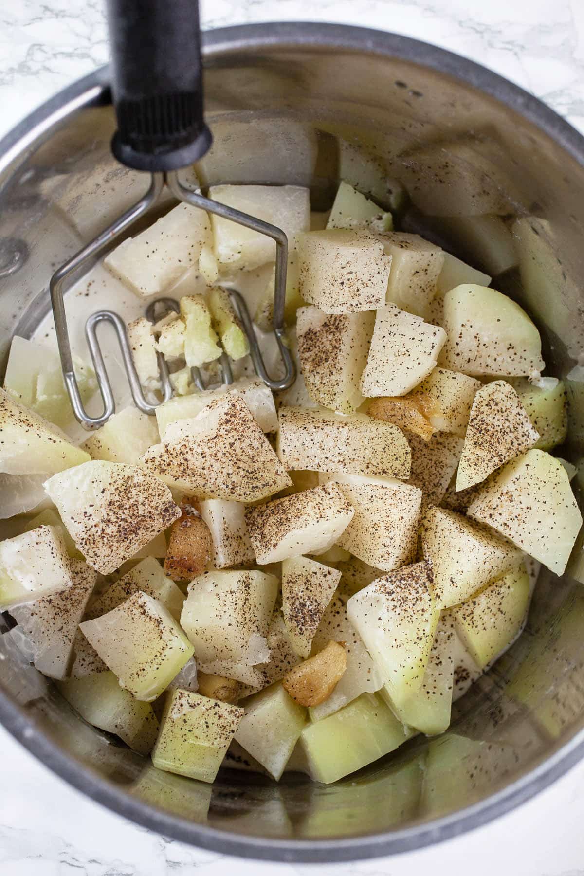 Cooked kohlrabi, roasted garlic, and cream in pot with masher.