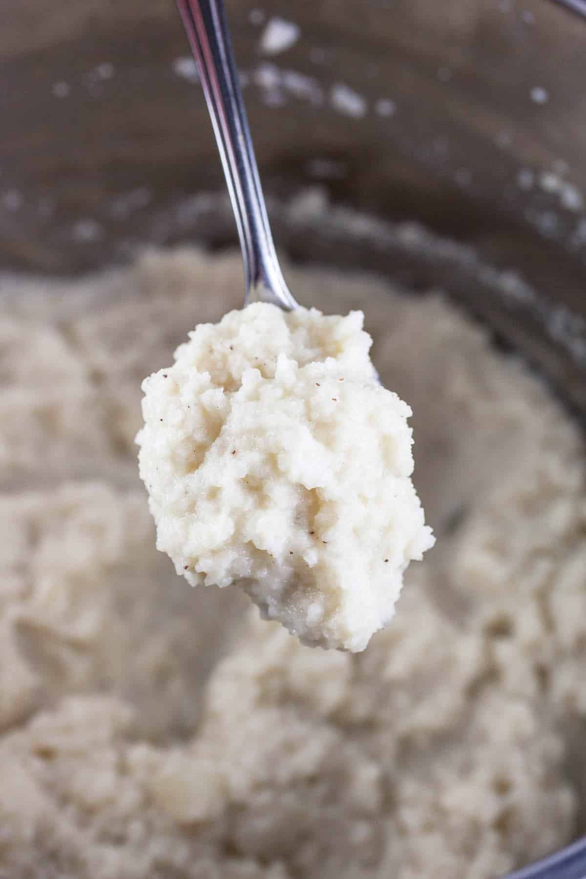 Spoonful of mashed kohlrabi lifted from pot.