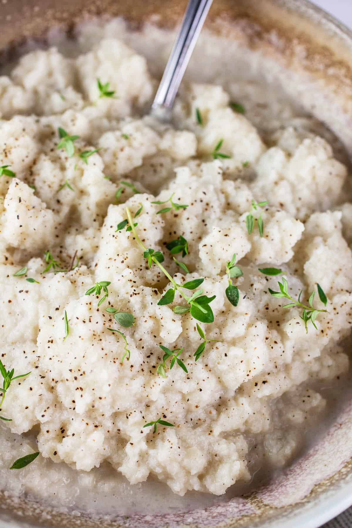 Mashed kohlrabi with fresh thyme in ceramic bowl.