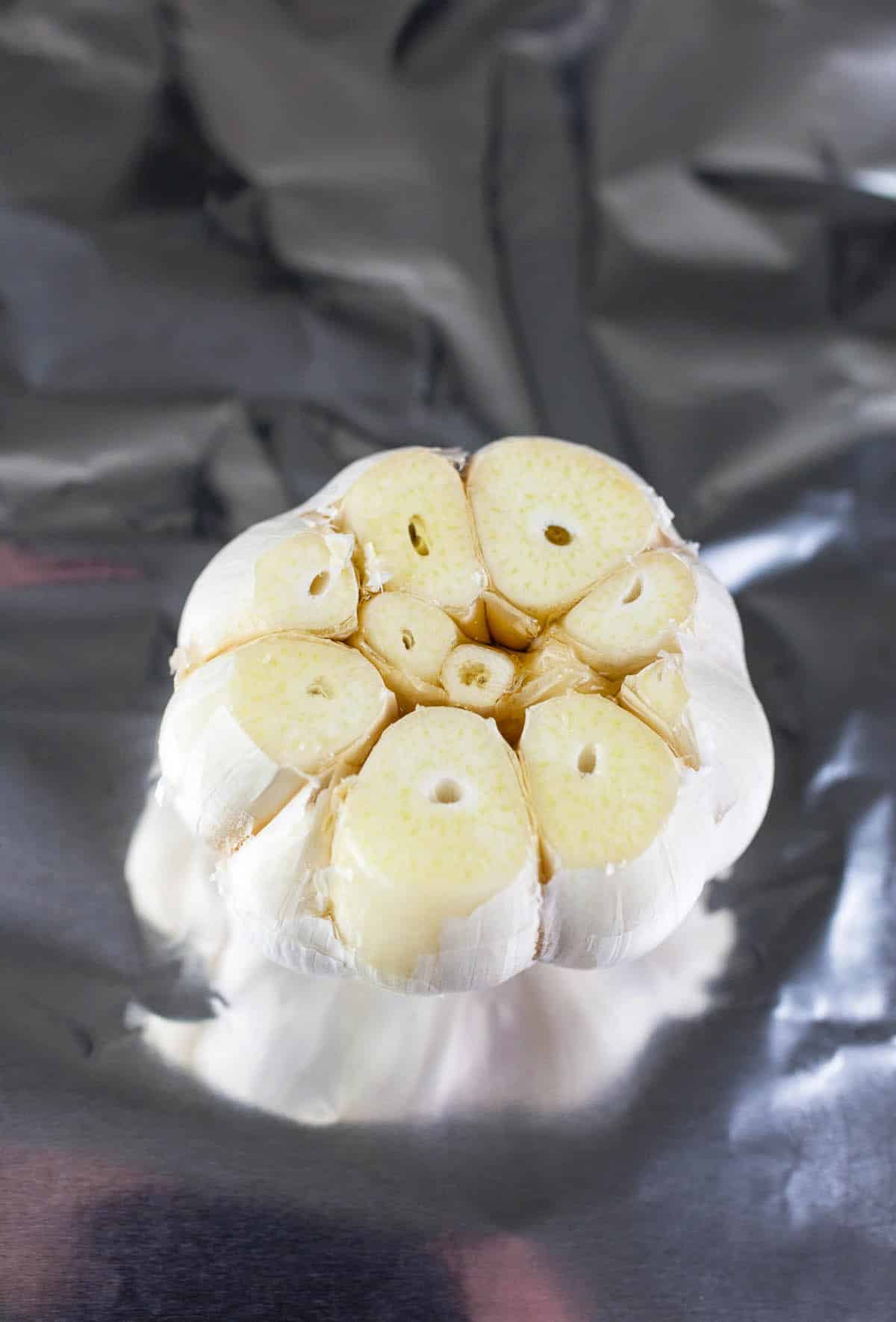 Head of raw garlic with top removed on tinfoil.