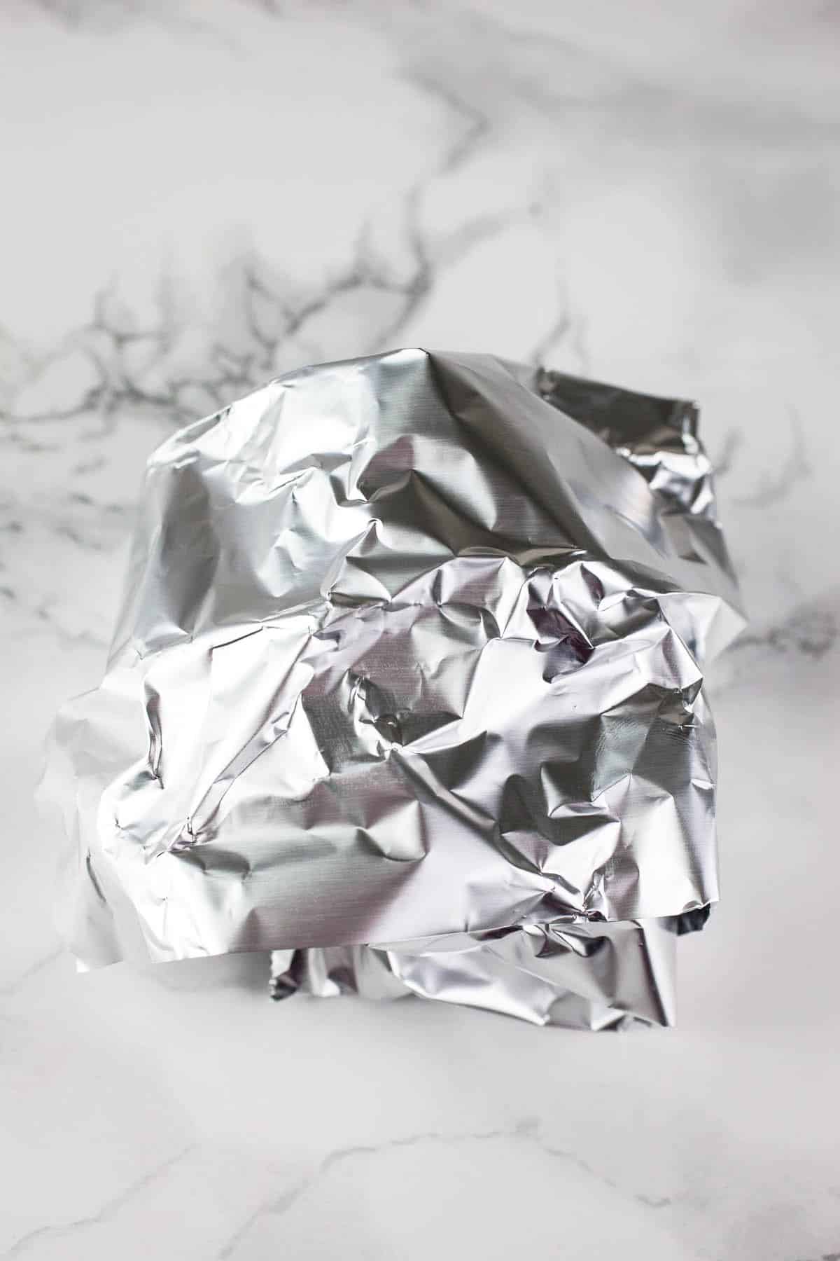 Garlic wrapped in tinfoil on white surface.