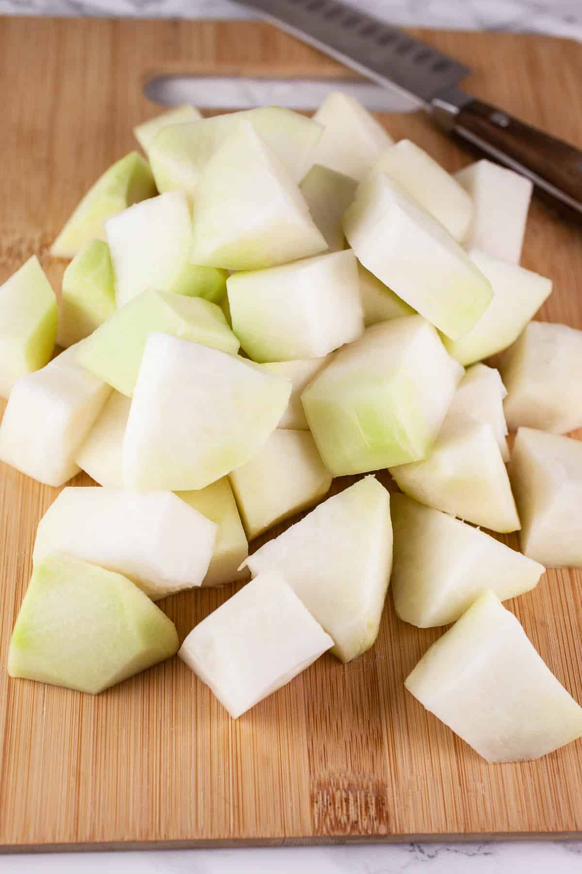 Kohlrabi chunks on wooden cutting board with knife.