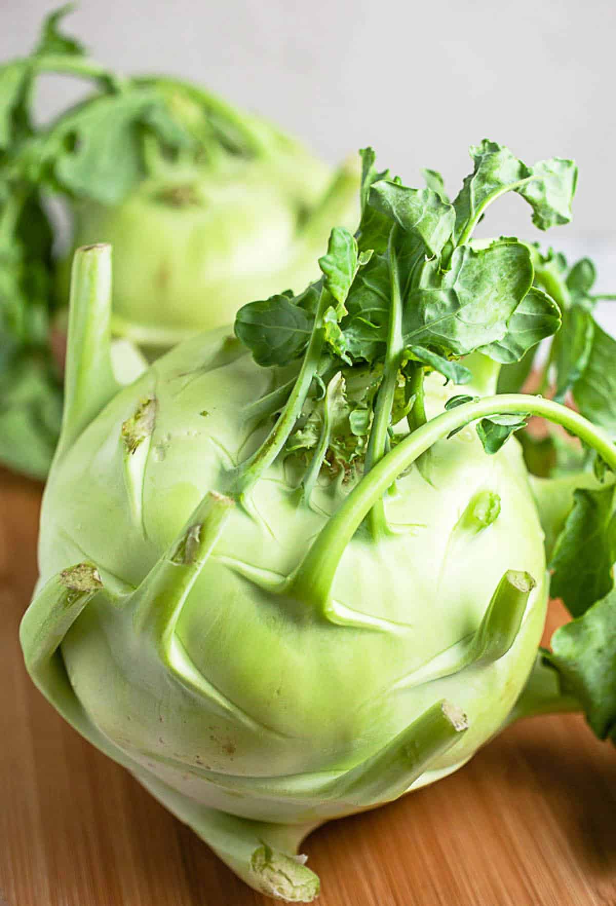 Whole kohlrabi on wooden cutting board.