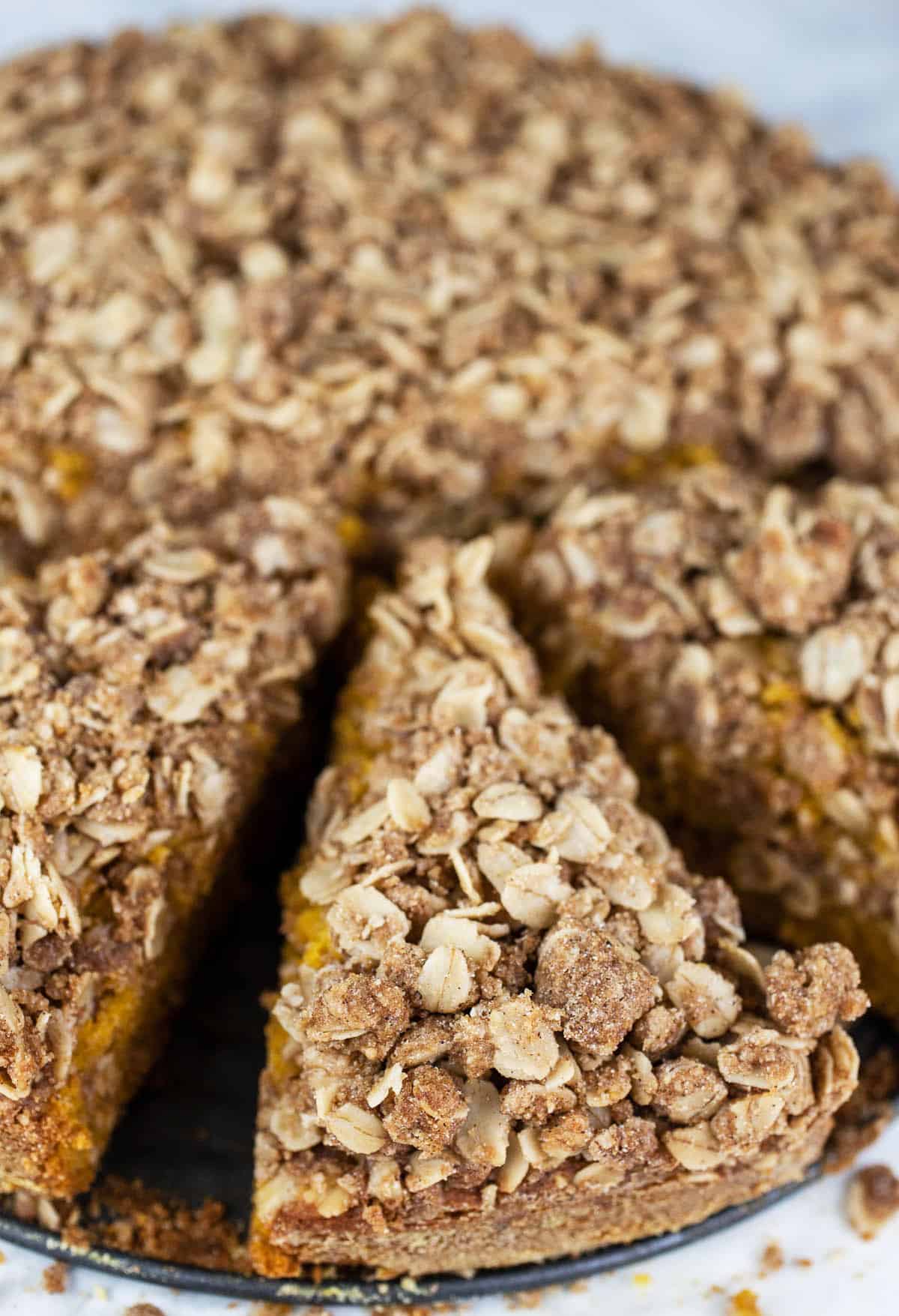 This Pumpkin Coffee Cake with Oatmeal Struesel Topping is the perfect fall breakfast or dessert! It's moist and fluffy, easy to make, and topped with a sweet cinnamon oatmeal streusel topping. This pumpkin coffee cake recipe is made from scratch and is great for Thanksgiving, the holidays, or all year round. Crumbly struesel is the best! So good with a cup of coffee! #ad #flahavans #oatspiration #pumpkin #coffeecake #oatmeal Sliced pumpkin streusel coffee cake.