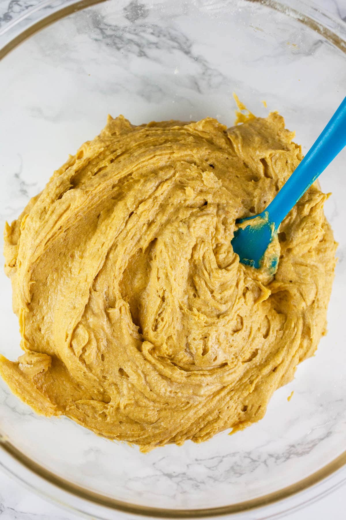 Pumpkin coffee cake batter in large glass bowl with blue spatula.