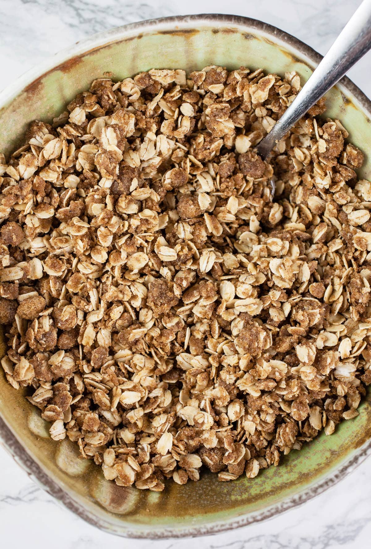 This Pumpkin Coffee Cake with Oatmeal Struesel Topping is the perfect fall breakfast or dessert! It's moist and fluffy, easy to make, and topped with a sweet cinnamon oatmeal streusel topping. This pumpkin coffee cake recipe is made from scratch and is great for Thanksgiving, the holidays, or all year round. Crumbly struesel is the best! So good with a cup of coffee! #ad #flahavans #oatspiration #pumpkin #coffeecake #oatmeal Oatmeal streusel topping in ceramic bowl with spoon.