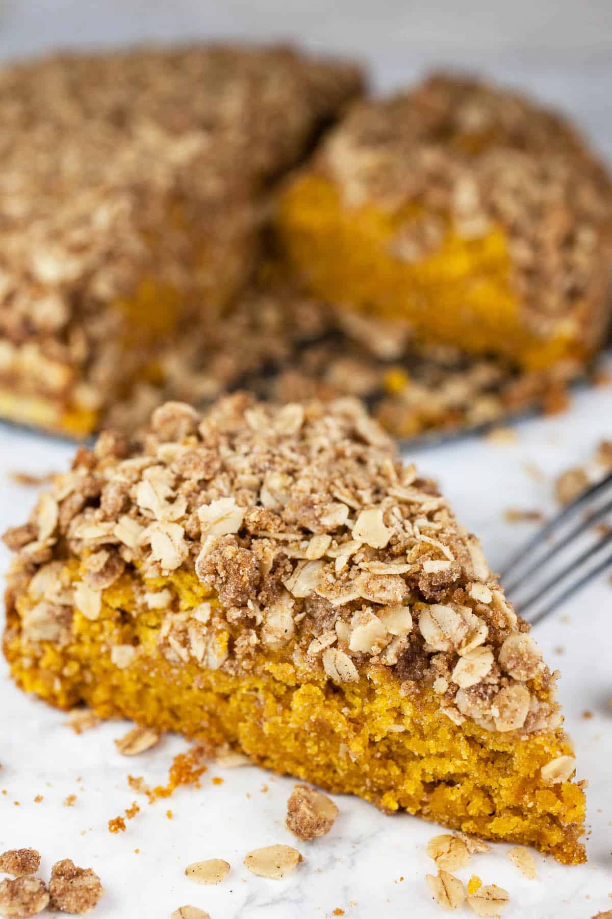 This Pumpkin Coffee Cake with Oatmeal Struesel Topping is the perfect fall breakfast or dessert! It's moist and fluffy, easy to make, and topped with a sweet cinnamon oatmeal streusel topping. This pumpkin coffee cake recipe is made from scratch and is great for Thanksgiving, the holidays, or all year round. Crumbly struesel is the best! So good with a cup of coffee! #ad #flahavans #oatspiration #pumpkin #coffeecake #oatmeal Slice of pumpkin coffee cake with fork.