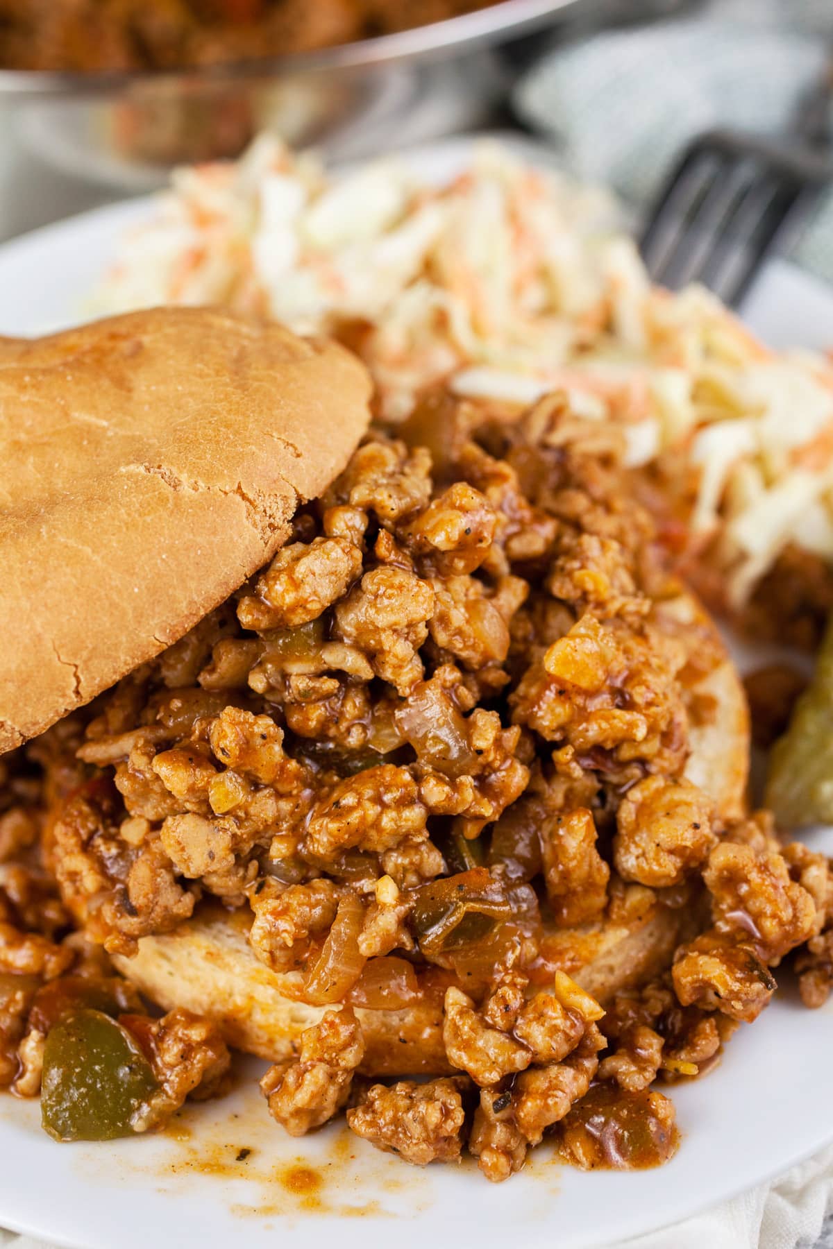 BBQ ground chicken sloppy joes with coleslaw and pickle on white plate.