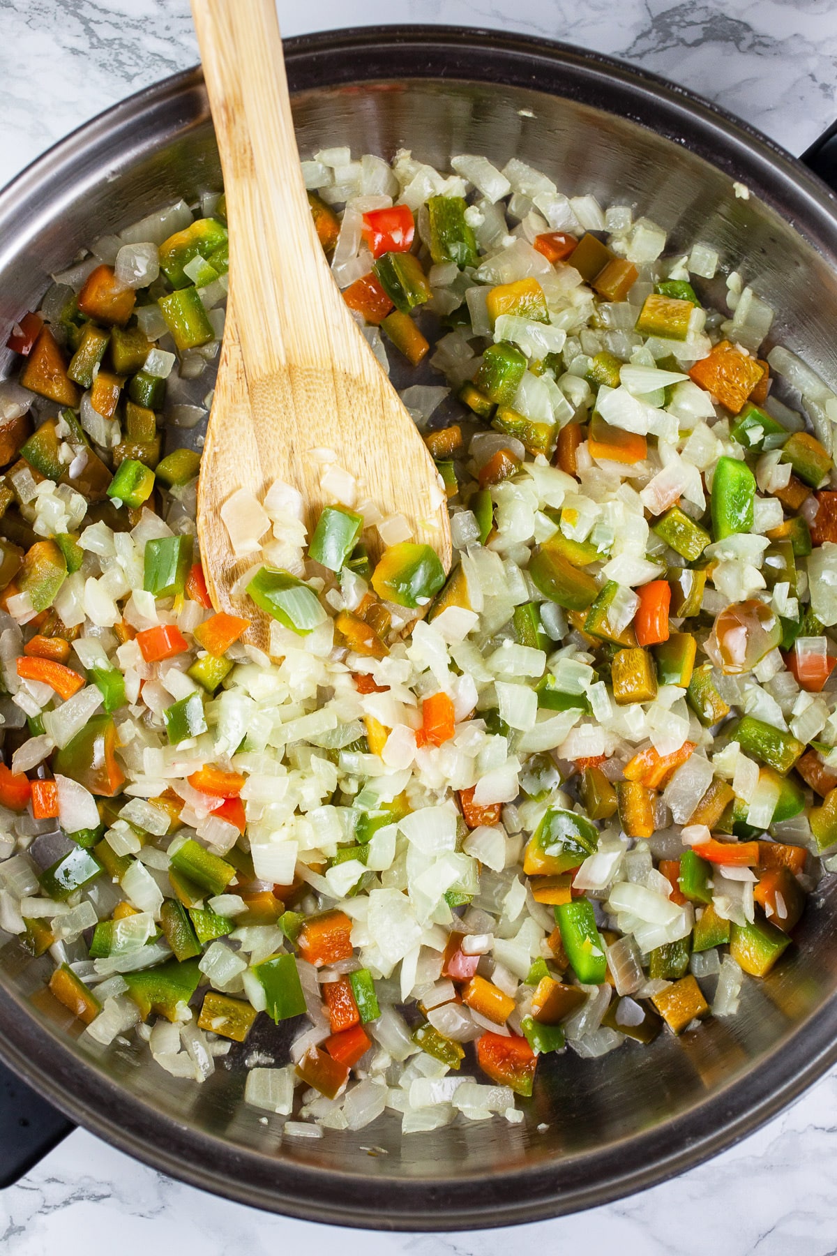 Garlic, onions, and peppers sautéed in skillet with wooden spoon.