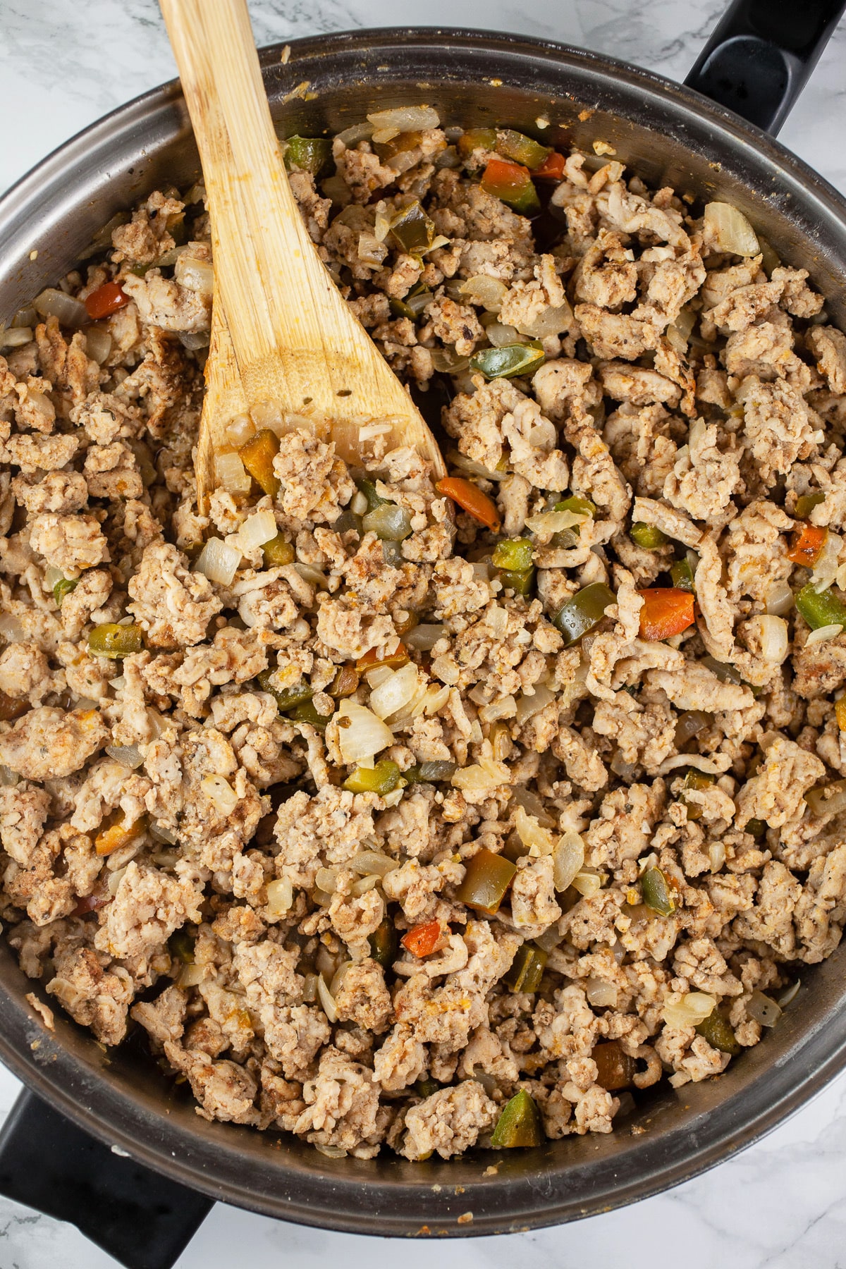 Ground chicken sautéed in skillet with wooden spoon.