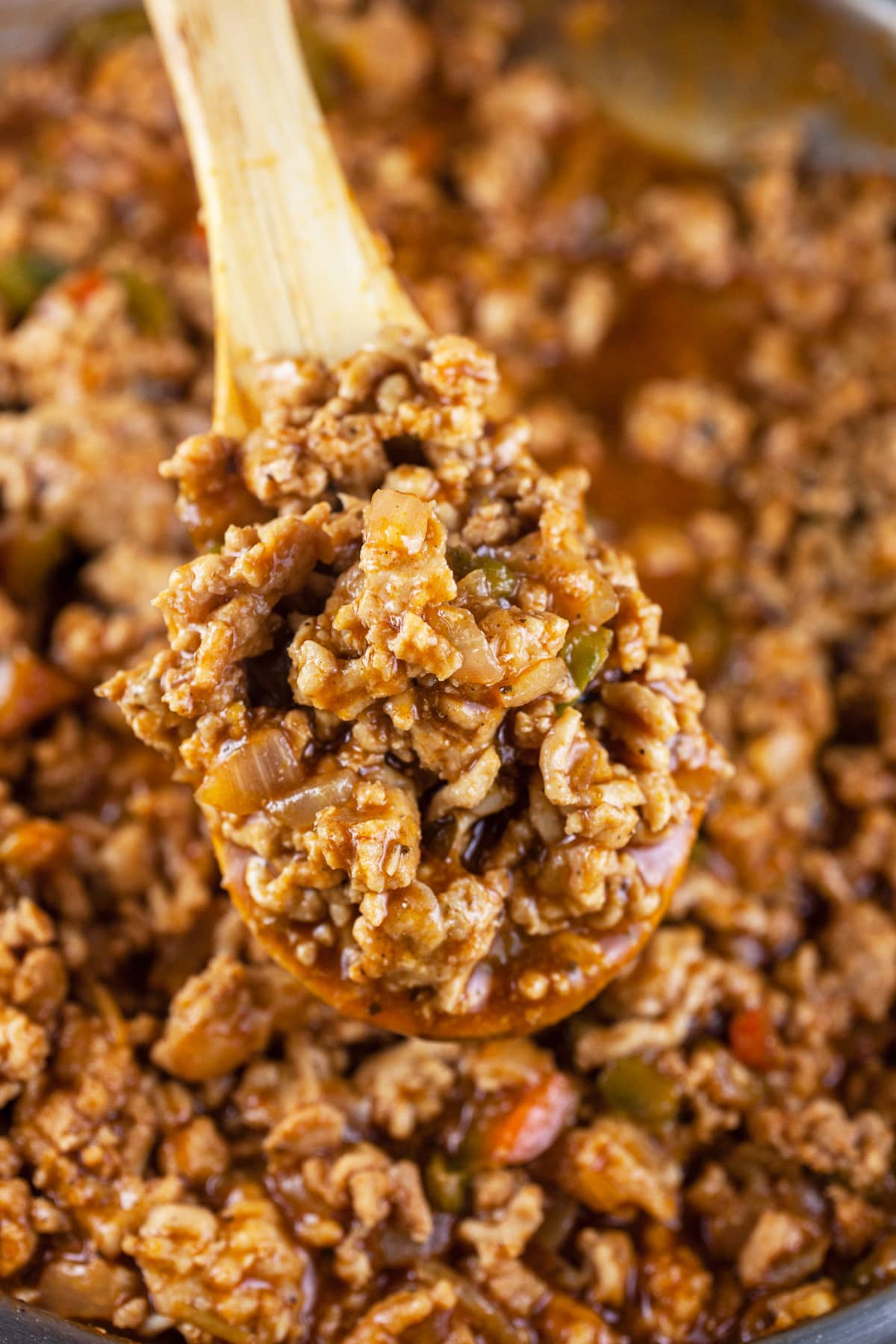 Scoop of sloppy joes lifted from skillet on wooden spoon.