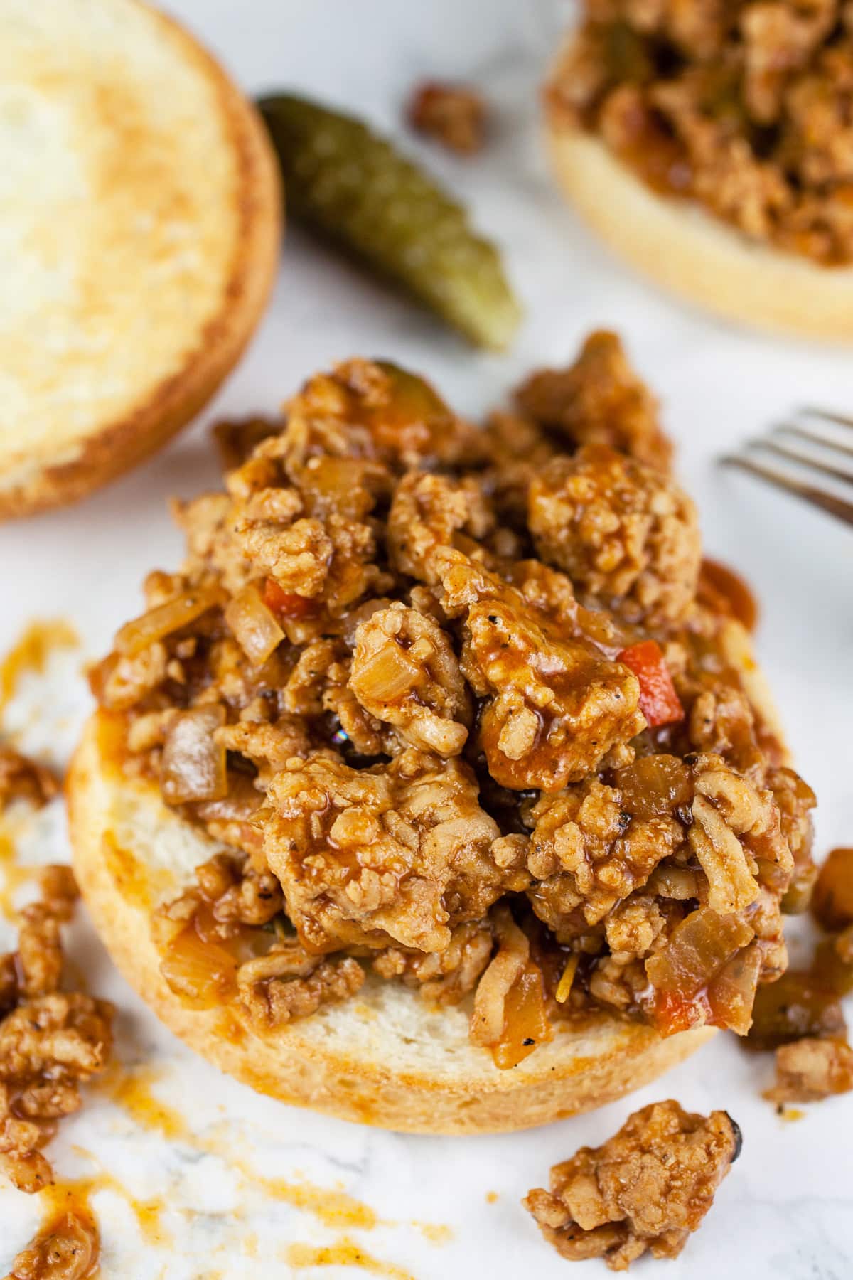 Open faced ground chicken sloppy joes on buns with pickle.