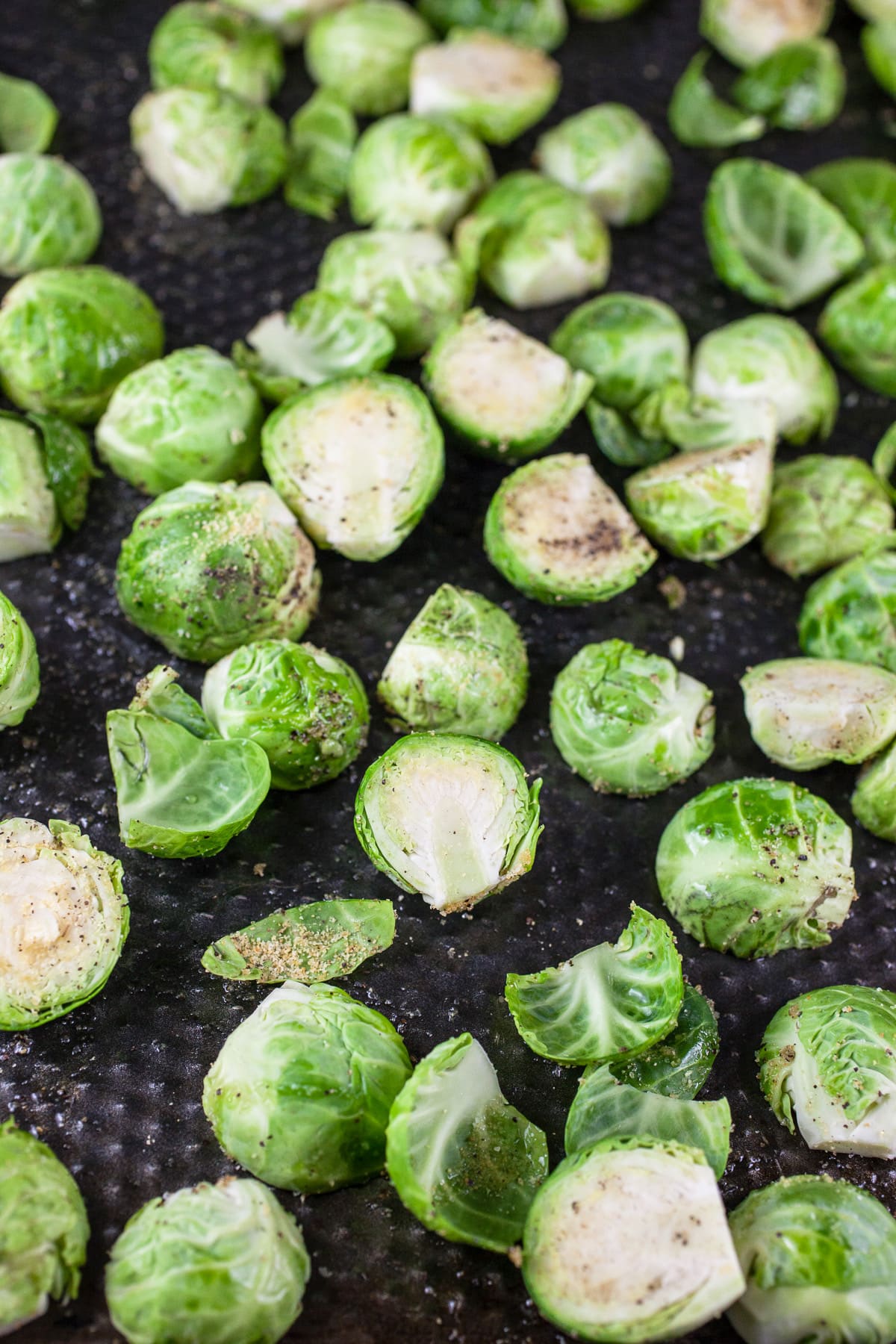 Raw Brussels sprouts tossed in olive oil and spices on baking sheet.