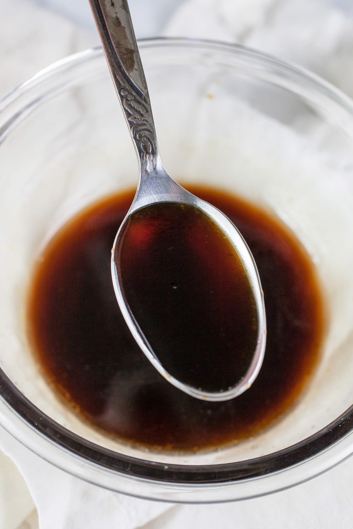 Maple sesame glaze on spoon lifted from small glass bowl.