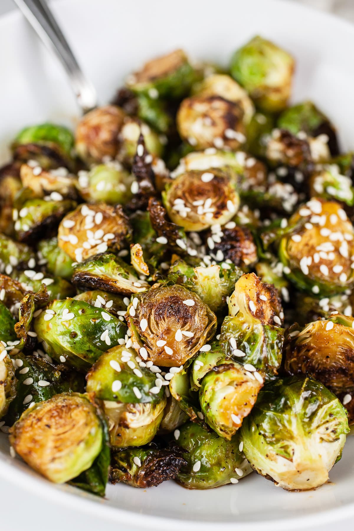 Maple sesame roasted Brussels sprouts in white bowl with fork.