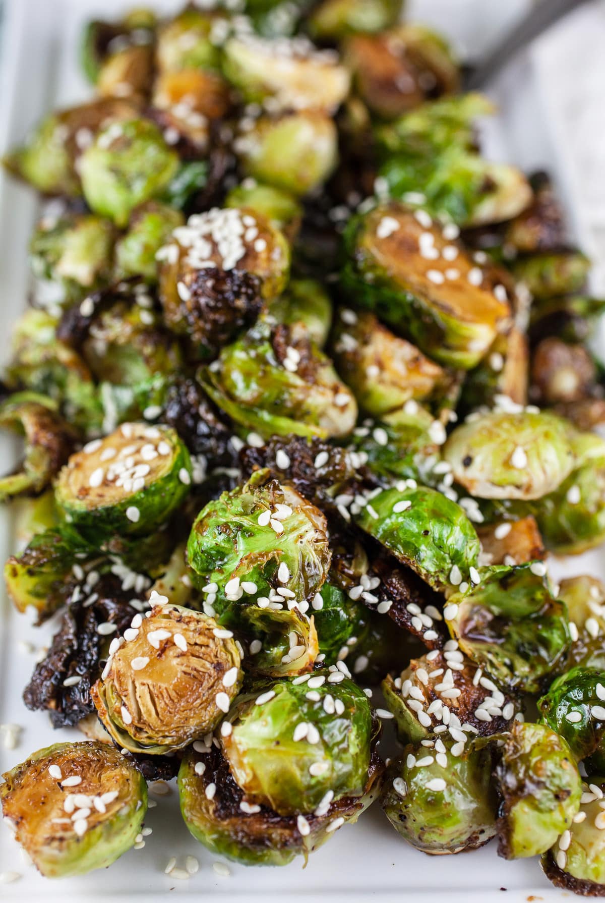 These Maple Sesame Roasted Brussels Sprouts make the perfect easy and healthy side dish! These Brussels sprouts are a little sweet and a little savory. The maple syrup and sesame oil totally compliment each other. This recipe is both vegetarian and vegan. A great addition to a Thanksgiving or holiday dinner menu! #brusselssprouts #vegetarian #vegan #maple #sesame Roasted Brussels sprouts with sesame seeds on white platter.