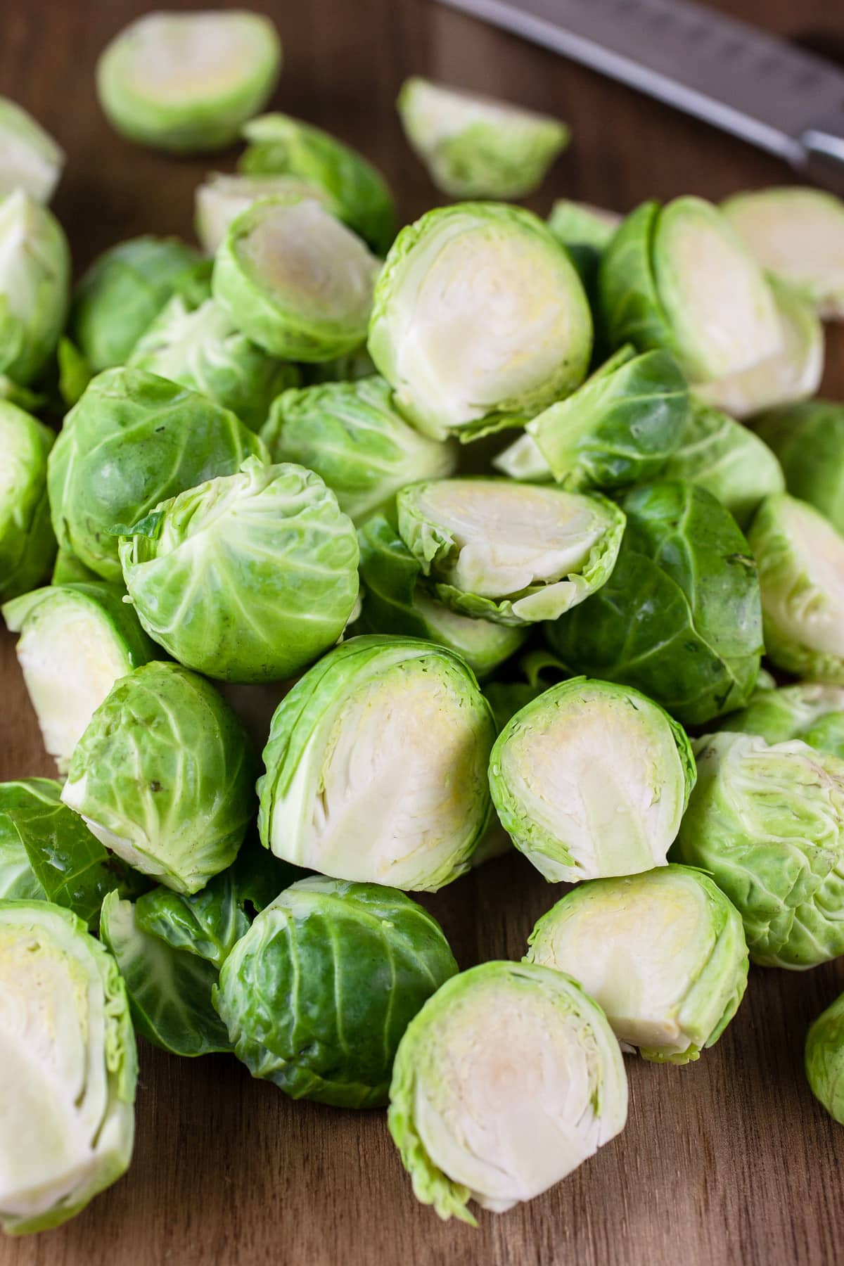 Chopped Brussels sprouts on wooden cutting board with knife.