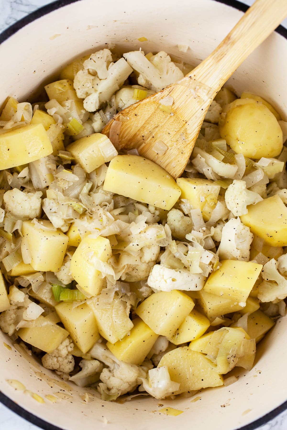 Leeks, garlic, onions, cauliflower, and potatoes sautéed in Dutch oven with wooden spoon.