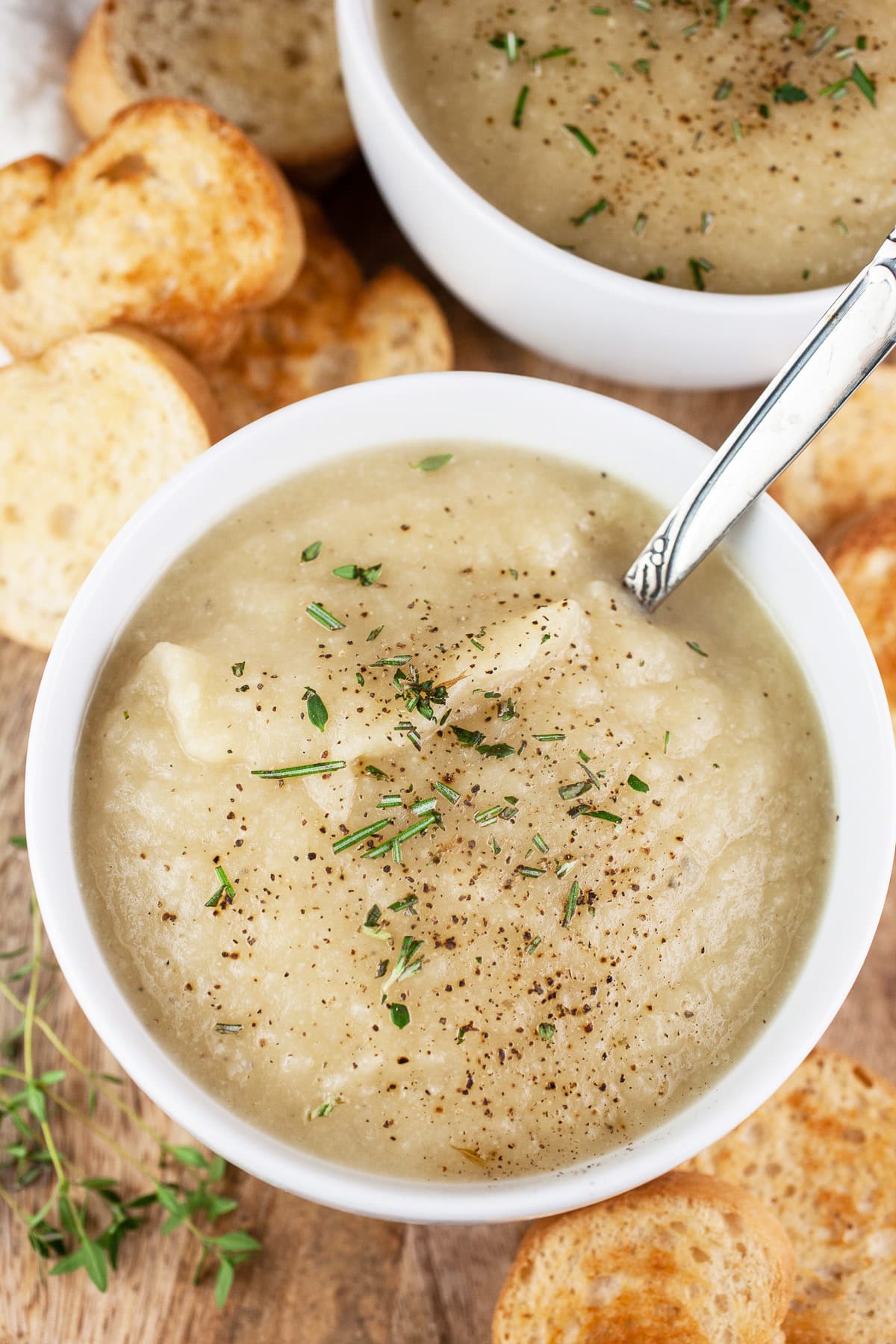 Potato leek cauliflower soup in white bowls with spoon and crostini.