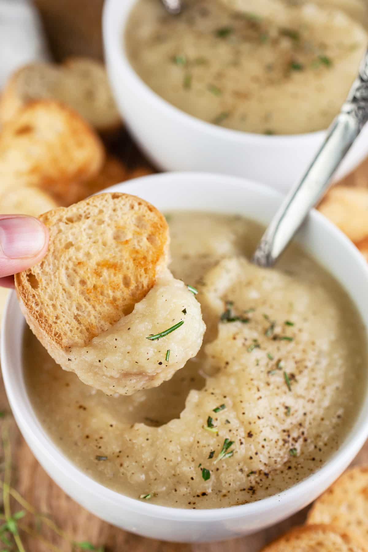 Crostini dipped into small white bowl of potato cauliflower leek soup.
