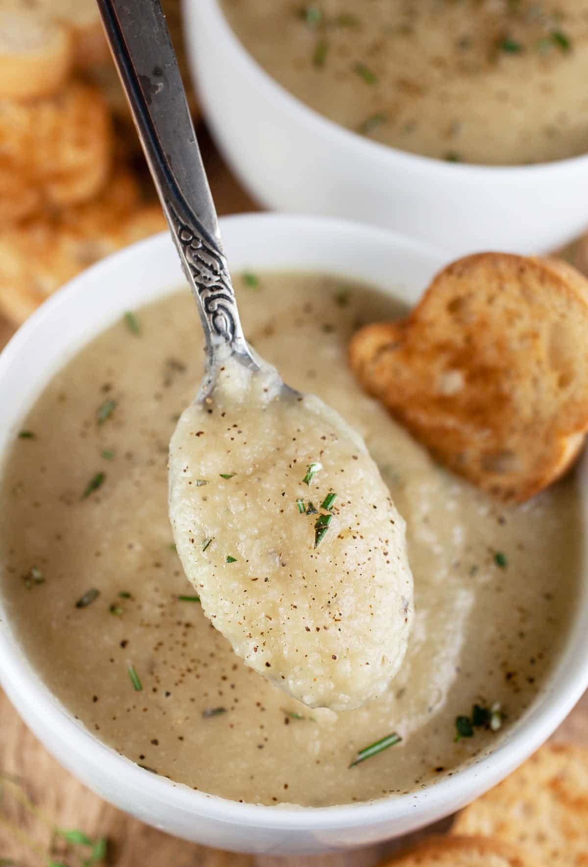 Spoonful of potato leek cauliflower soup lifted from white bowl.