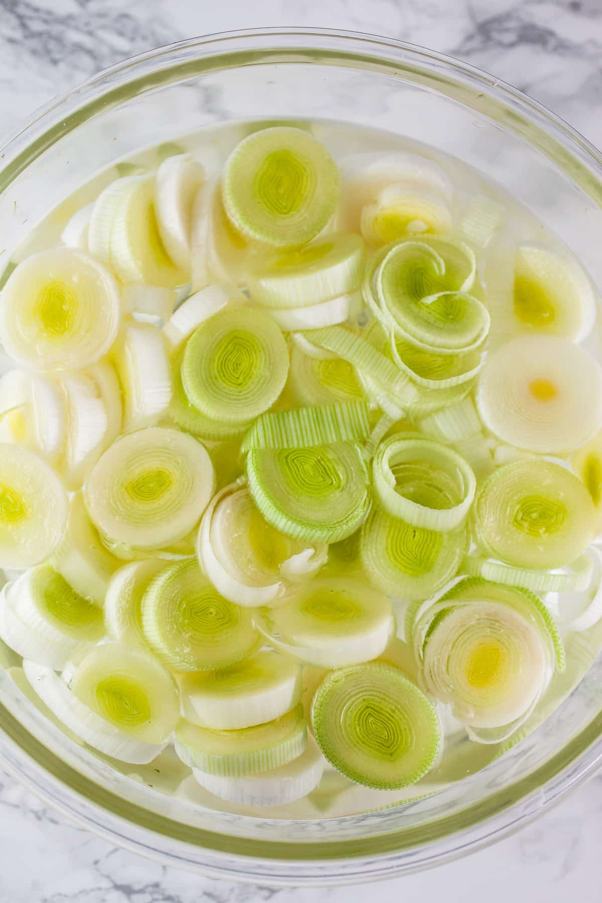 Chopped leeks in glass bowl full of water.