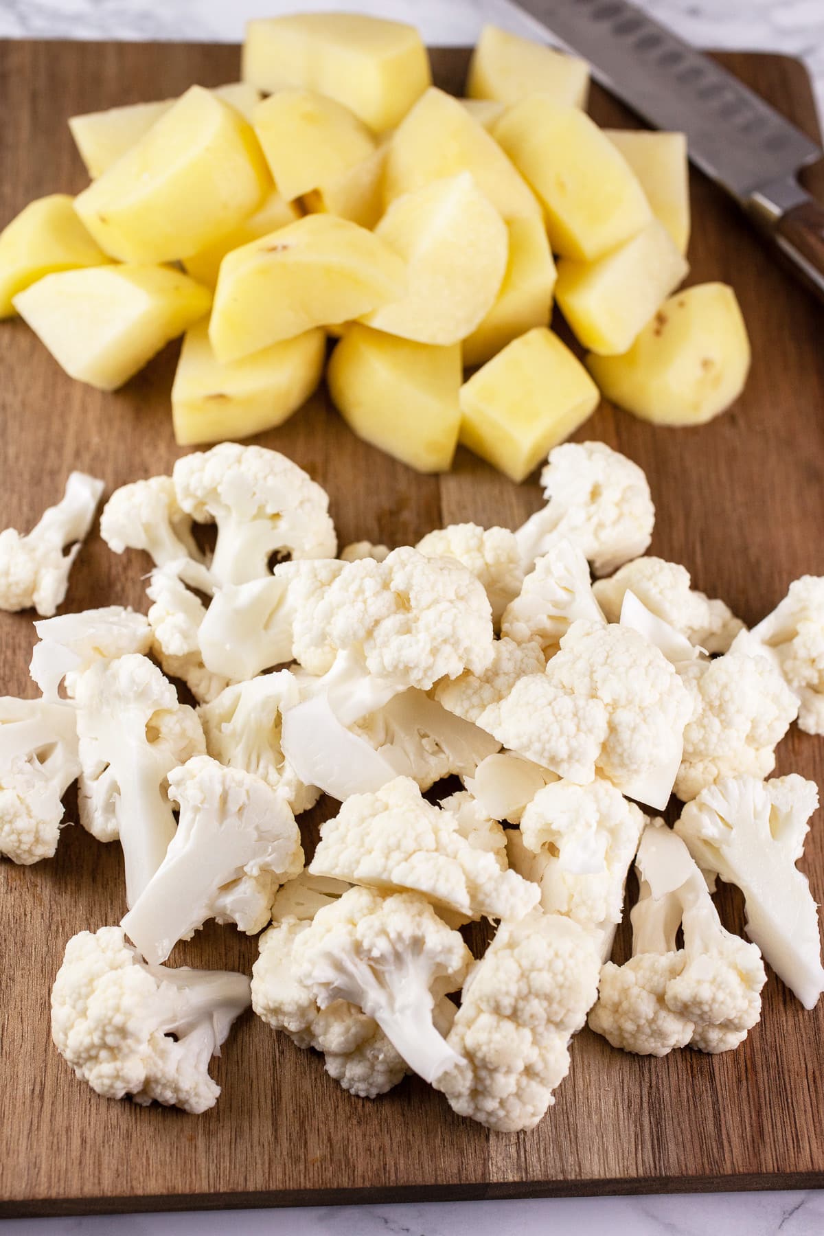 Cauliflower florets and diced potatoes on wooden cutting board.