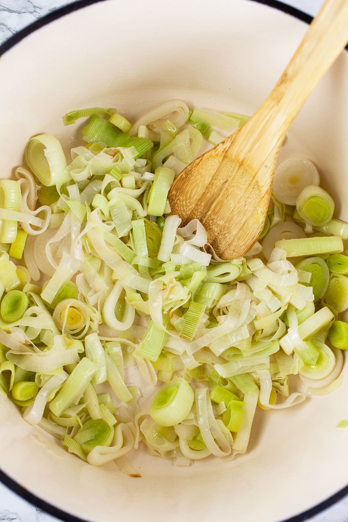 Leeks sautéed in Dutch oven with wooden spoon.