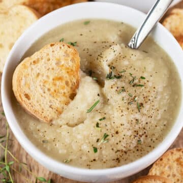Potato leek cauliflower soup with crostini in small white bowl.