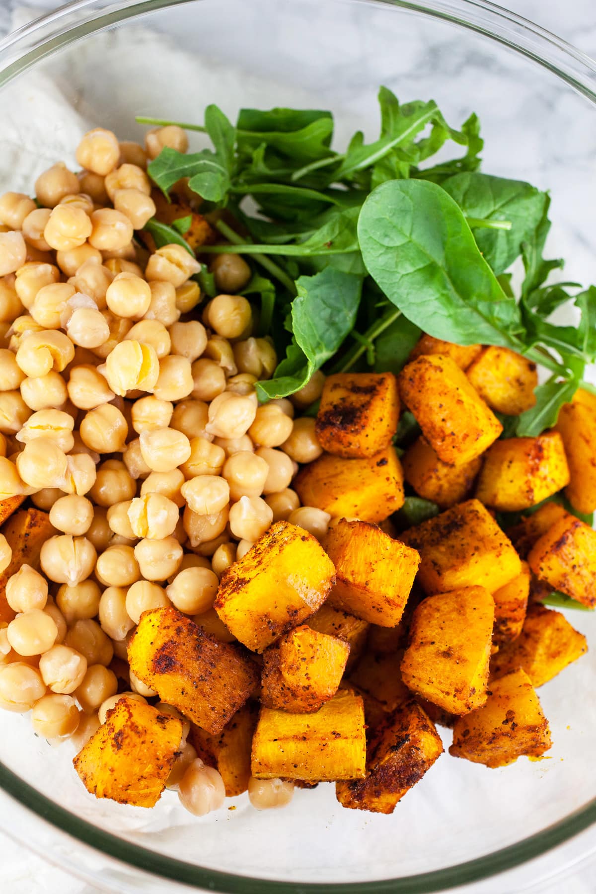 Roasted pumpkin, chickpeas, and greens in large glass bowl.