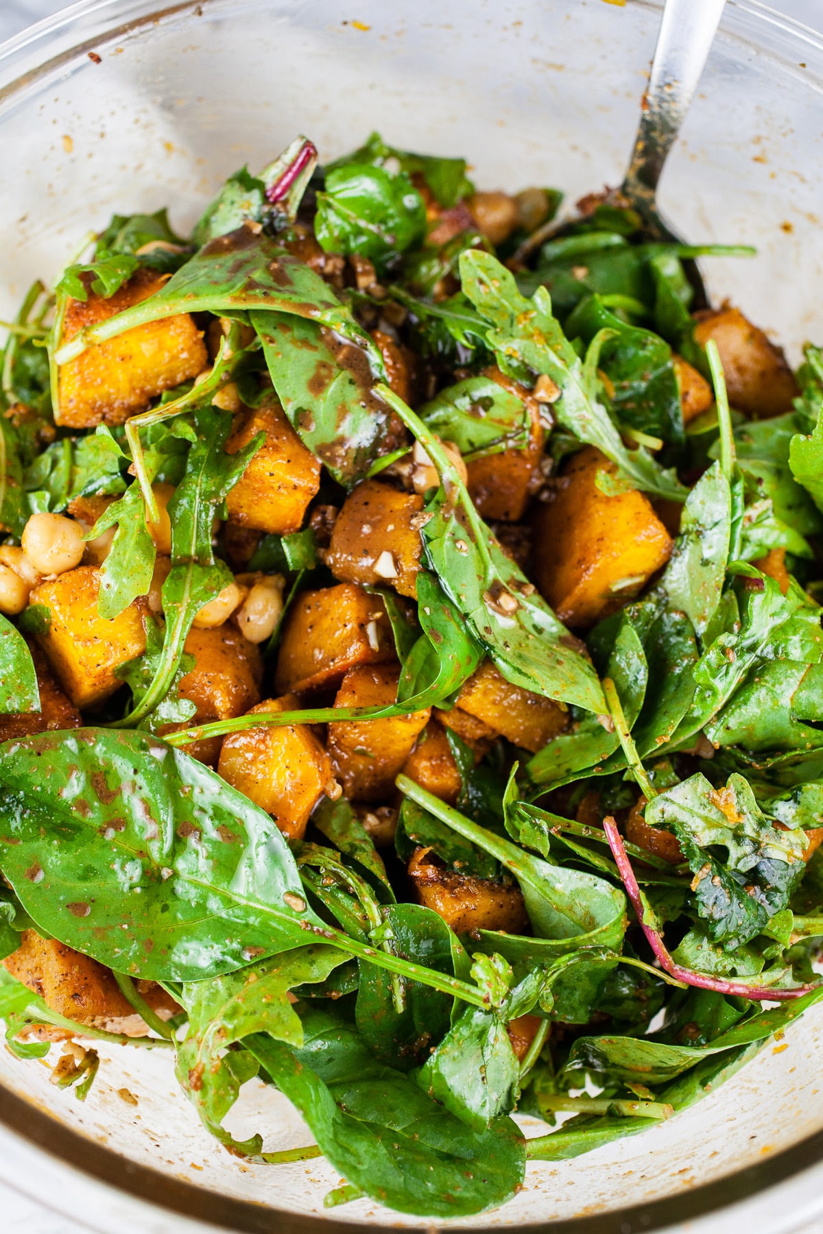 Roasted pumpkin, chickpeas, and greens tossed with balsamic dressing in large glass bowl.