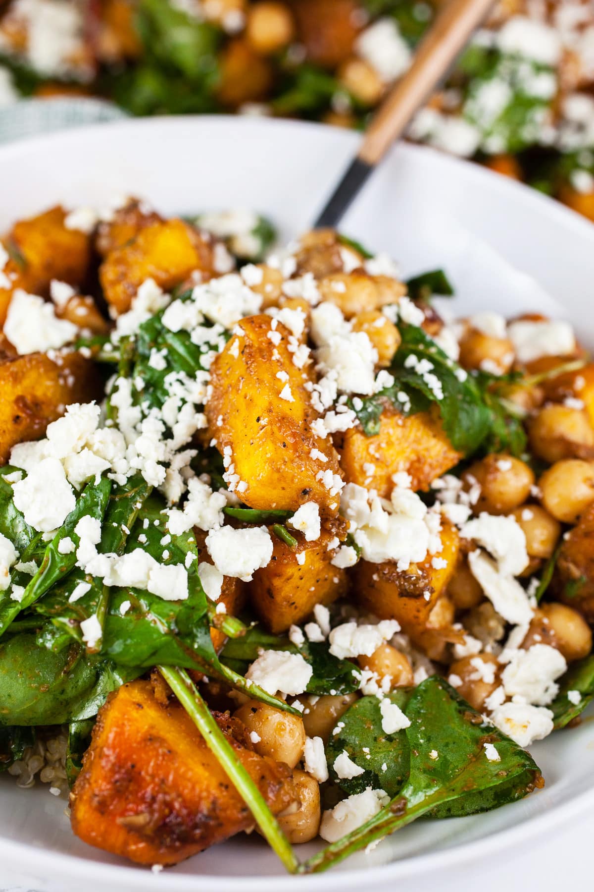 Pumpkin chickpea salad with feta in white bowl with fork.