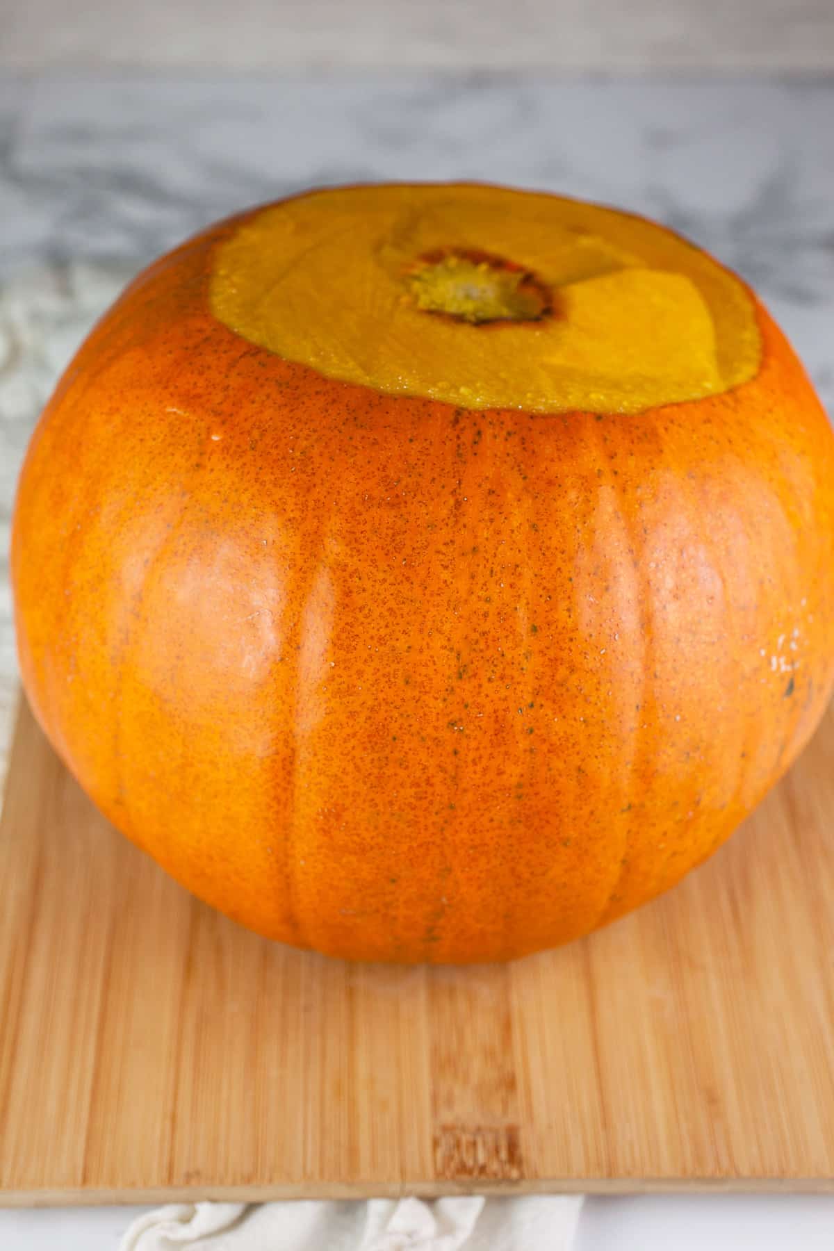 Pumpkin with stem removed on wooden cutting board.