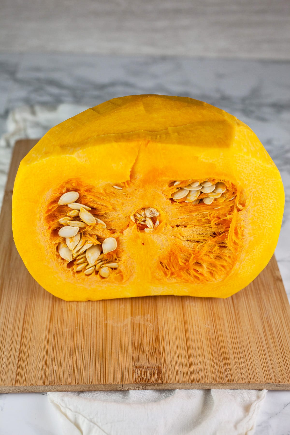 Peeled pumpkin cut in half with seeds on wooden cutting board.
