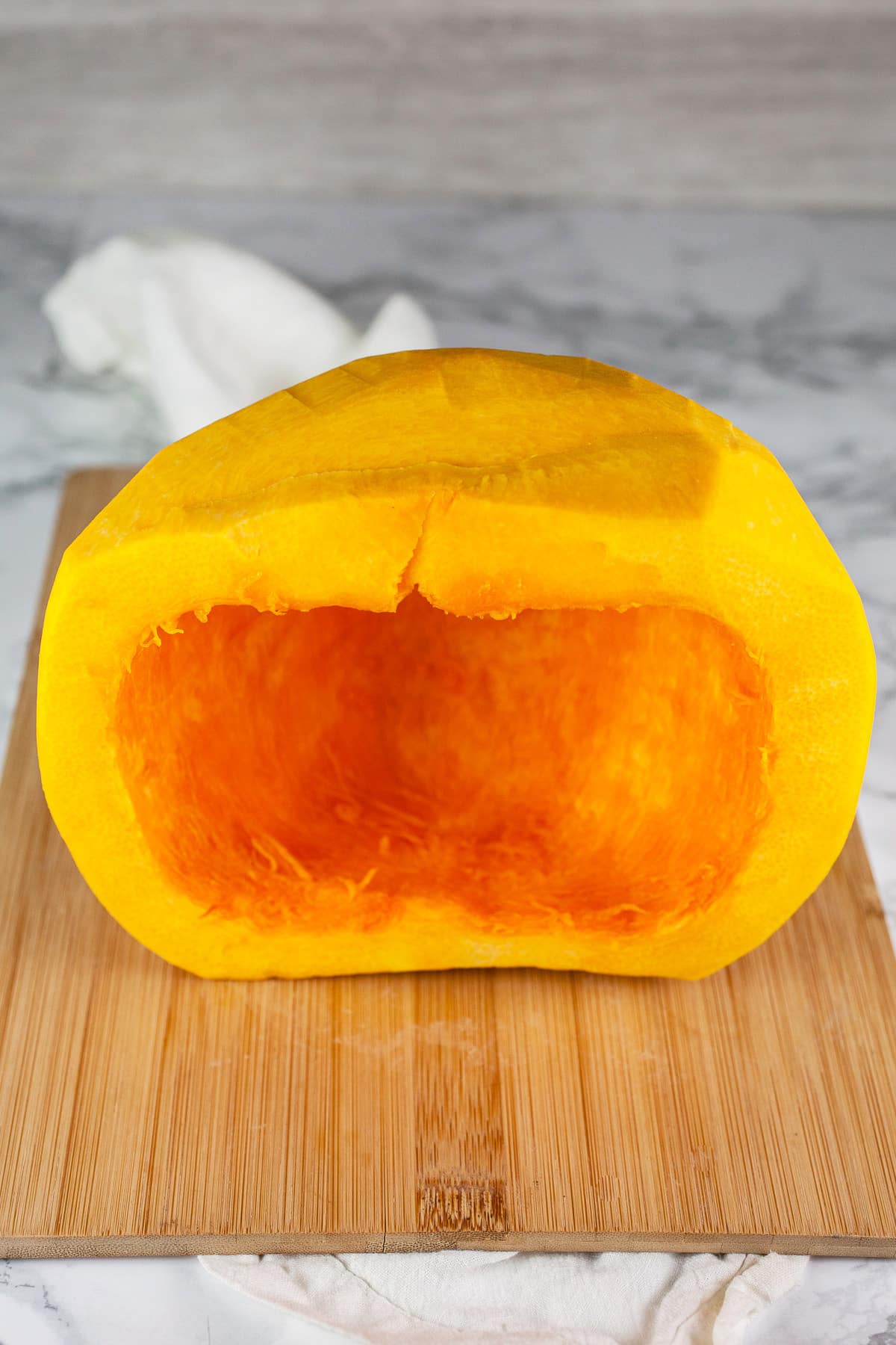 Peeled pumpkin cut in half with seeds removed on wooden cutting board.