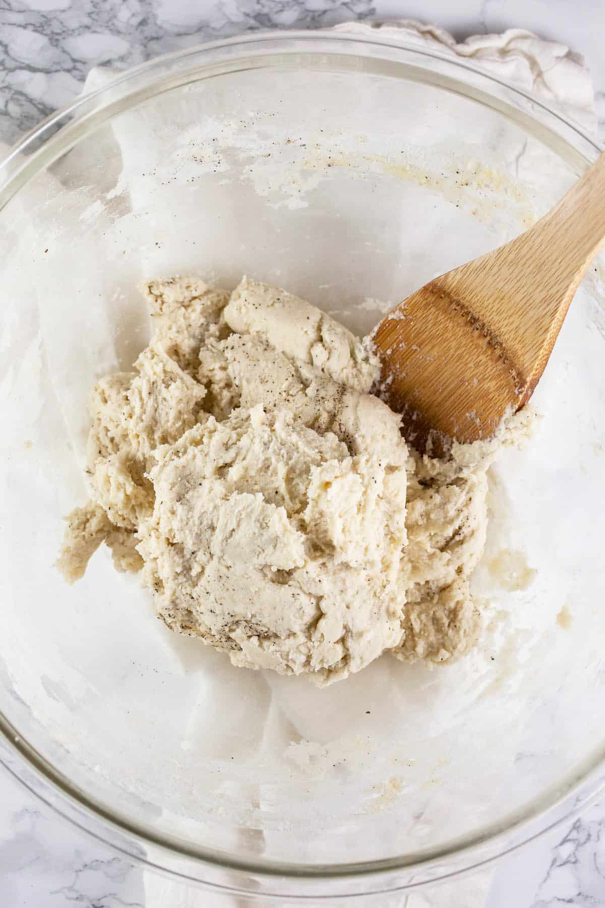 Dumpling batter in glass bowl with wooden spoon.