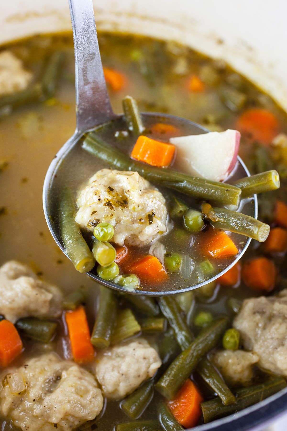 Scoop of vegetable stew lifted from Dutch oven on metal ladle.