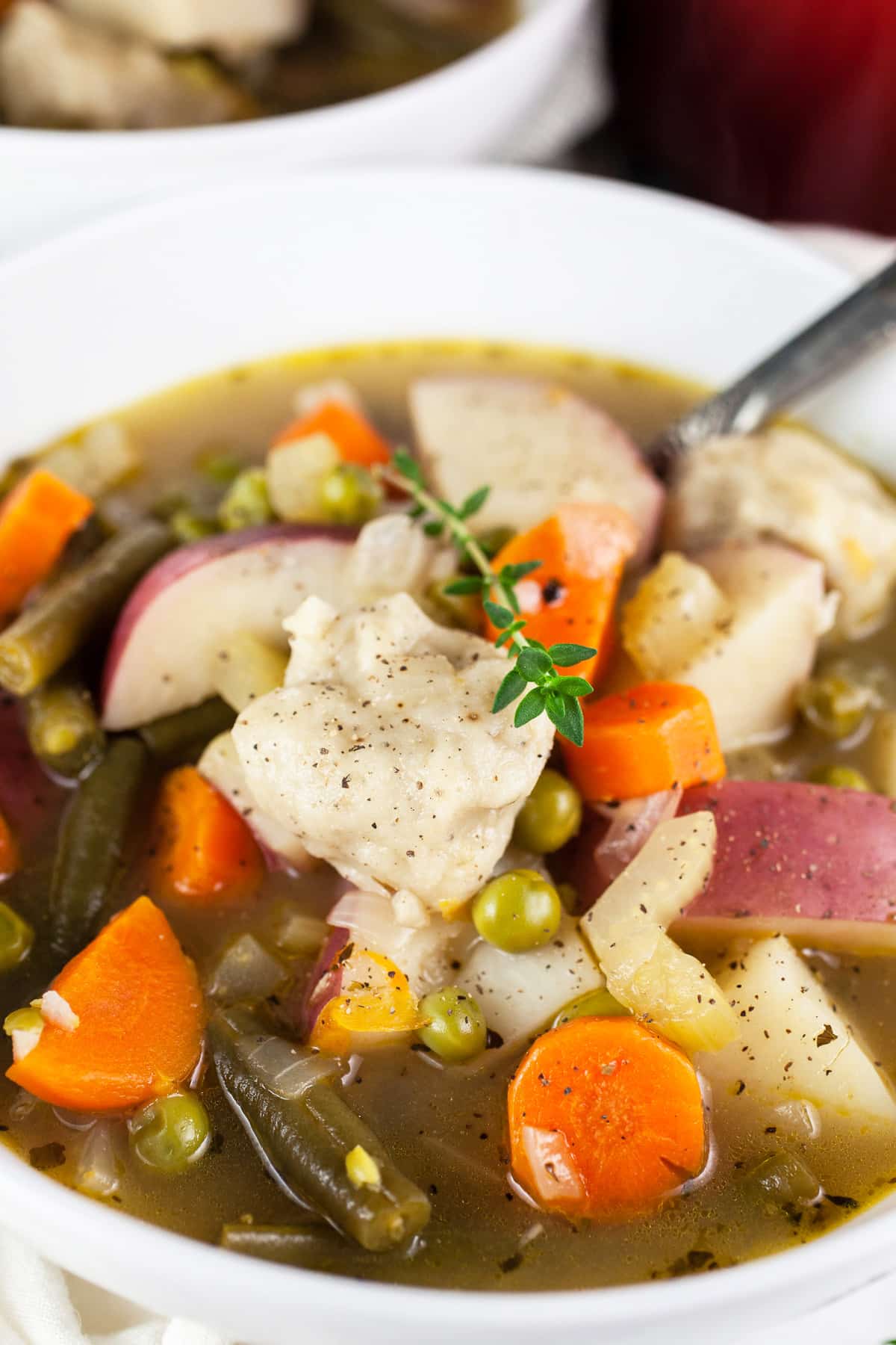 Veggie stew with dumplings in white bowl with spoon.