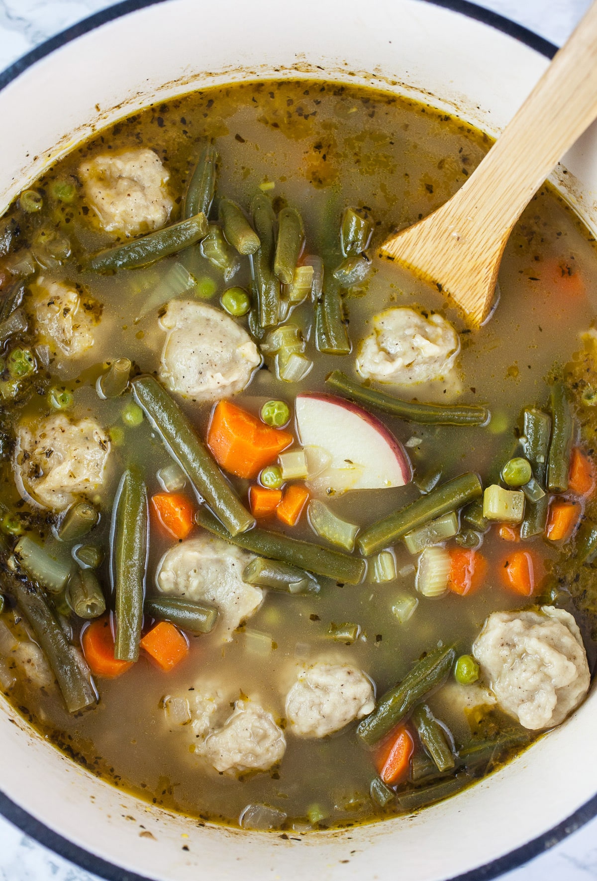 Veggie stew with dumplings in Dutch oven with wooden spoon.