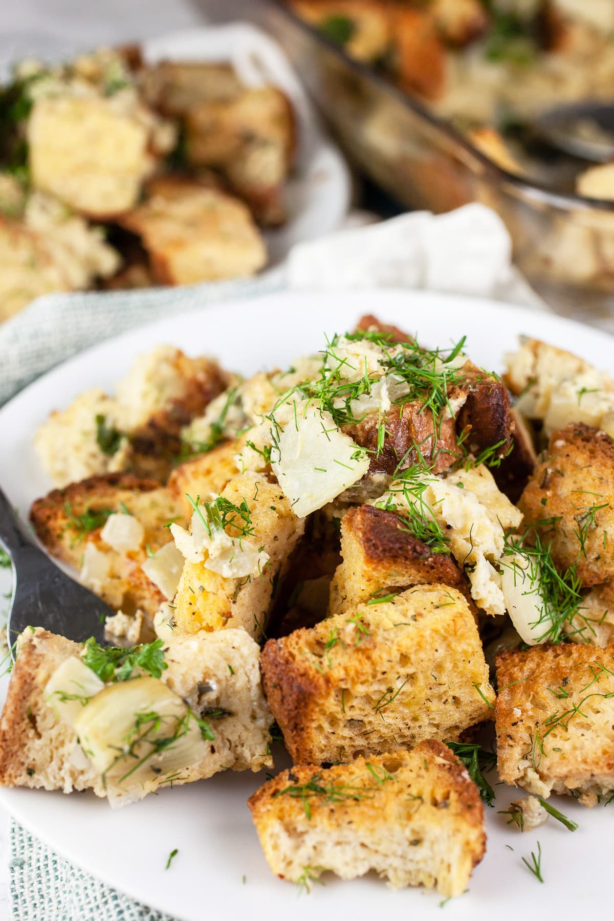 This Savory Fennel and Spinach Stuffing recipe is the perfect side dish for Thanksgiving dinner! It's healthy vegetarian comfort food at its best. This stuffing is made with toasted bread cubes and sauteed fennel. It's baked in the oven and super moist. This homemade stuffing is a unique take on a classic traditional dish. Stuffing from scratch is the best! #stuffing #fennel #spinach #thanksgiving #sides #recipes Fennel herb stuffing on white plate with fork.