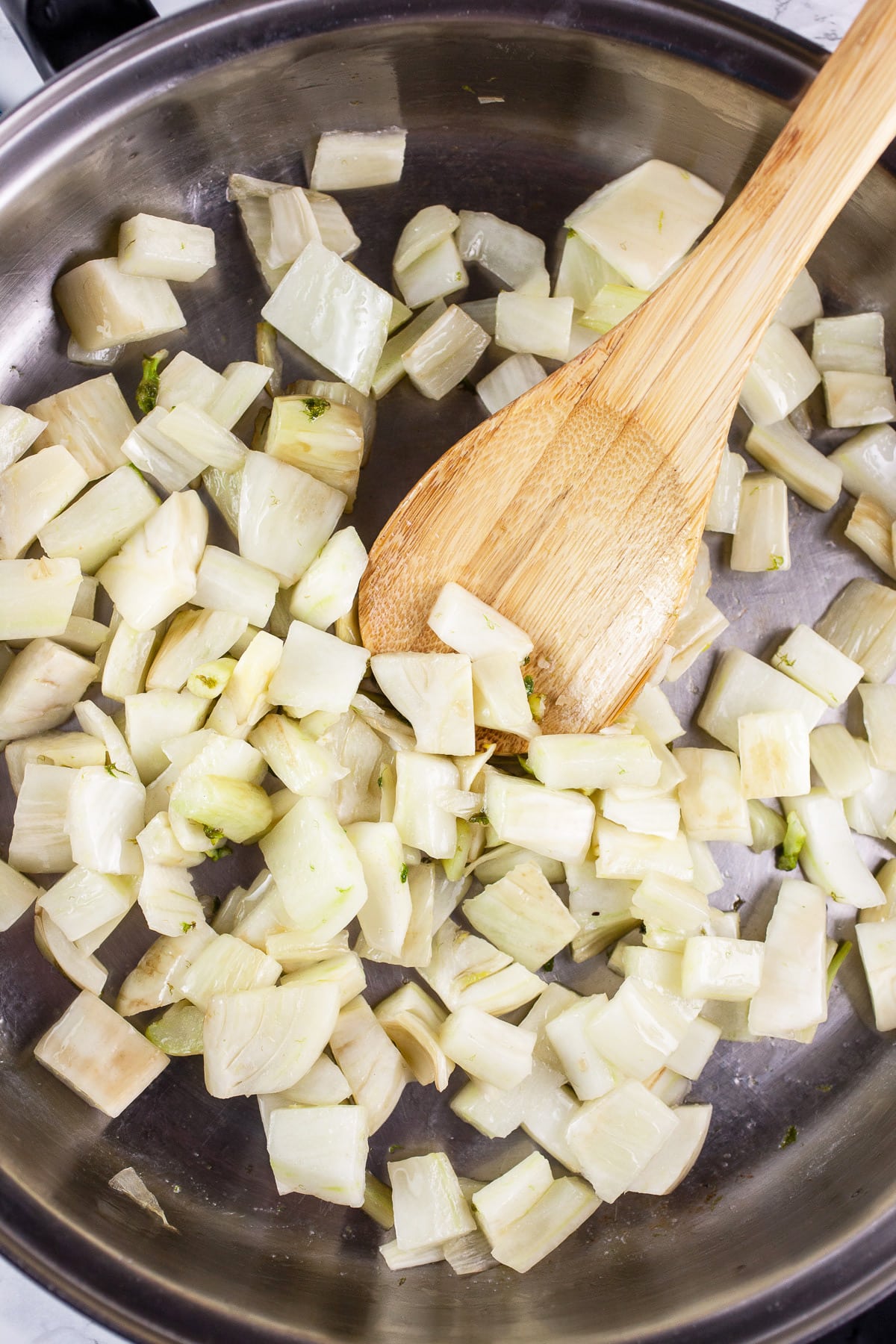 Fennel sautéed in skillet with wooden spoon.